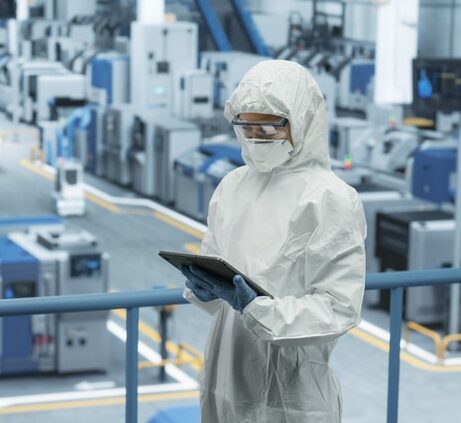 Female Technician in Protective Coveralls, Mask and Eyewear Using Tablet Computer at a Manufacturing Complex